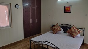 Een slaapkamer met een bed, twee kussens, een kledingkast, een klok, een raam en een plafondventilator.