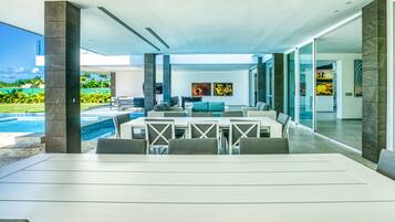 A modern outdoor dining area with a pool view, large windows, and contemporary furniture.