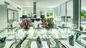 A modern dining area with a glass table set for a meal, surrounded by large windows offering a view of greenery. - Modern and Fresh Oceanfront Villa (Punta Cana)