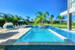 Una piscina rectangular con borde de azulejos, rodeada de sillas de descanso y una palmera.