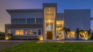 A modern two-story house with a large front porch, a stone facade, and a well-lit entrance. - Modern and Fresh Oceanfront Villa (Punta Cana)