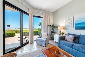 Relax in this stylish living room with a sofa, armchair, and coffee table, leading to an outdoor area through a large sliding glass door.