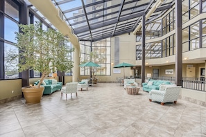 Relax in a spacious area with a glass roof, surrounded by seating and a lush potted tree.