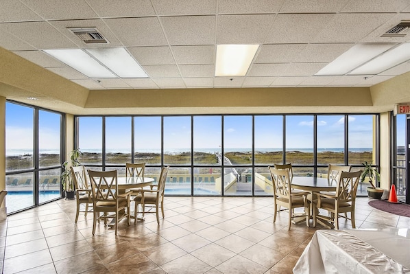 Enjoy a panoramic ocean view from the room's large windows, featuring a single bed and dining area with round tables and chairs.