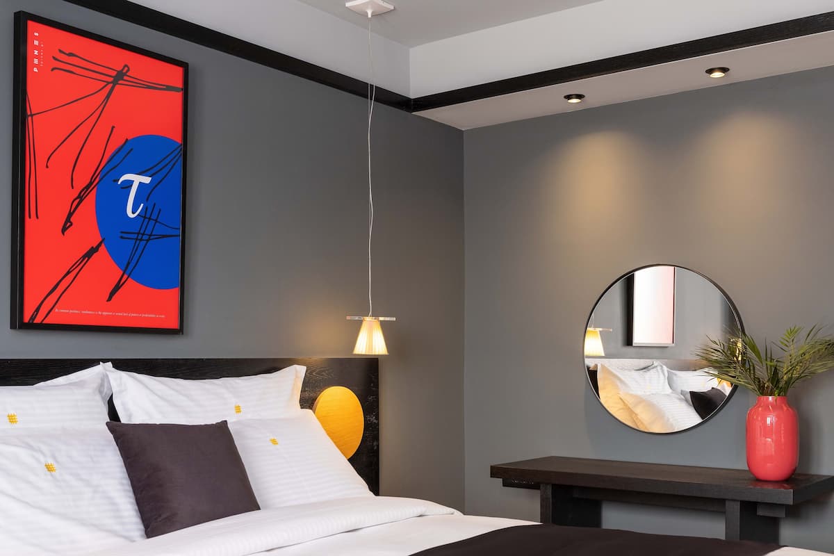 A modern bedroom with a bed, a bedside table, a mirror, and a wall art piece.