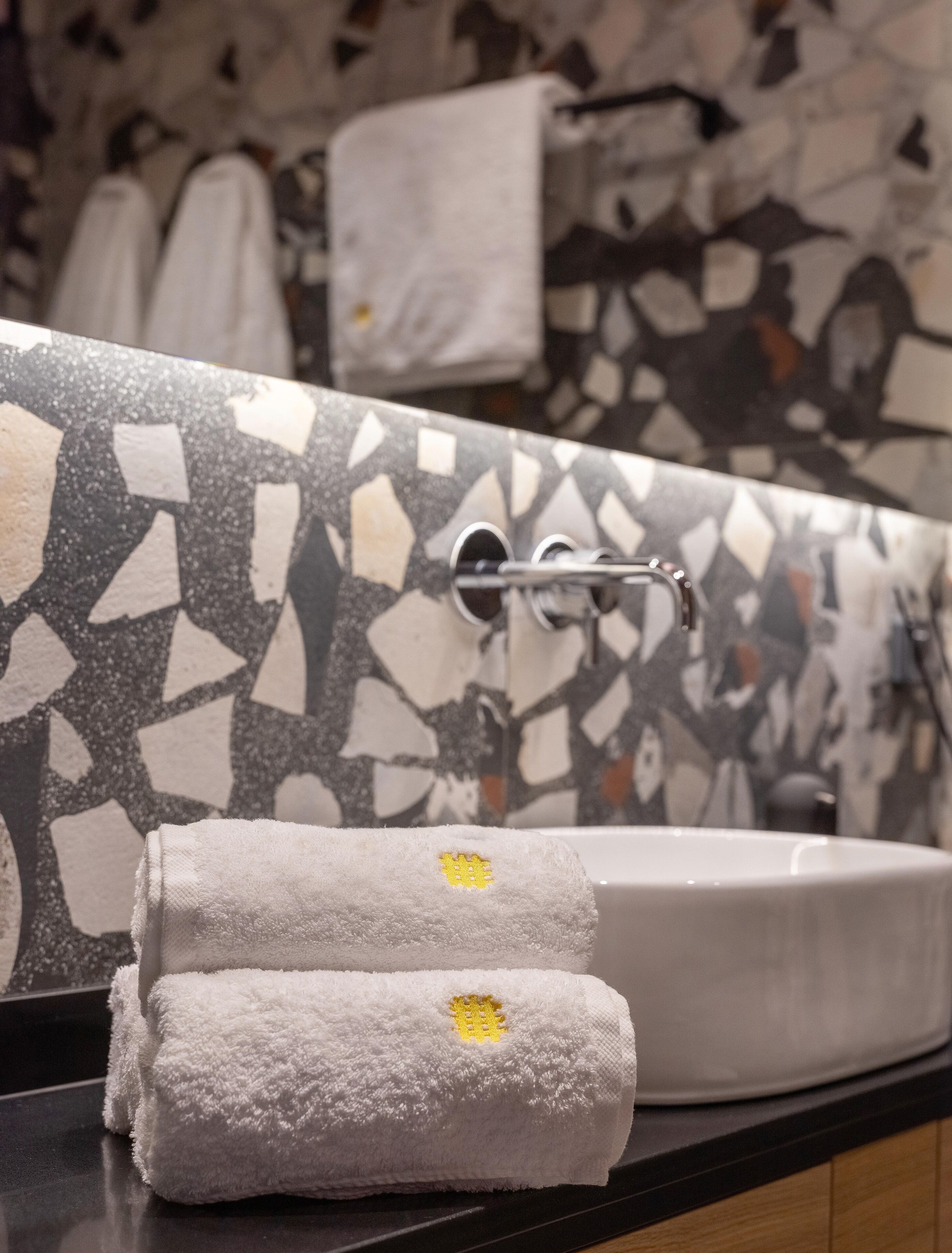 A bathroom with a mosaic tile wall, a sink, and two towels with a yellow emblem.