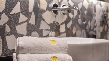 Un baño con pared de mosaicos, un lavamanos y dos toallas con un emblema amarillo.