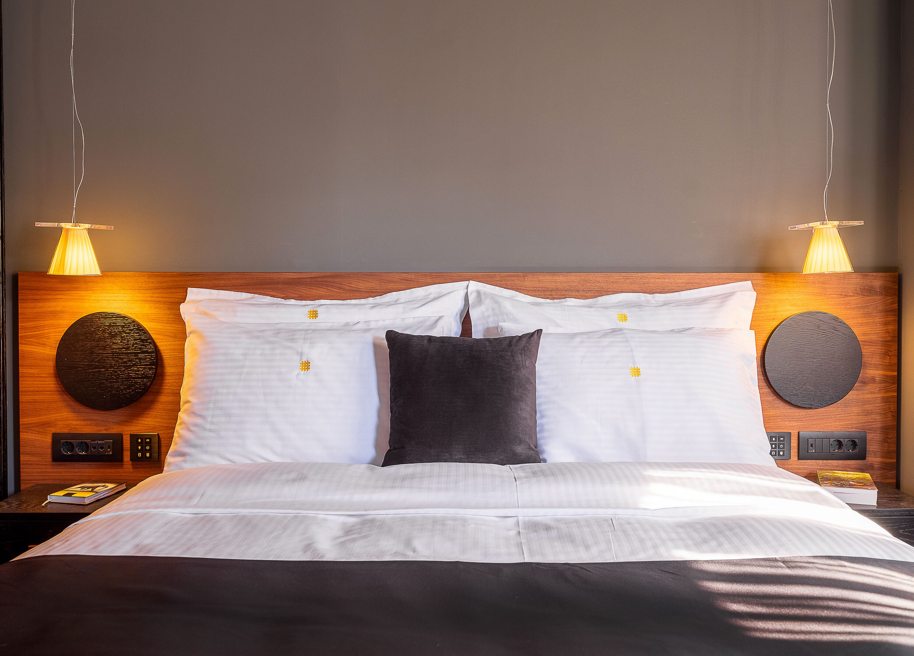 A neatly made bed with white and dark pillows, a wooden headboard, and two bedside lamps.