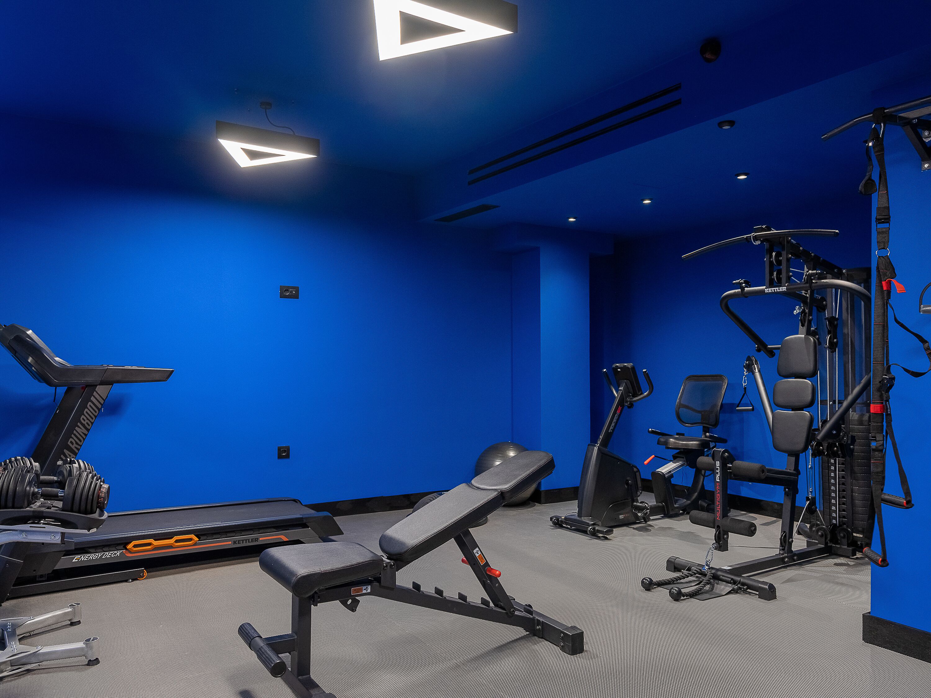 A gym with exercise equipment, a treadmill, and a bench.