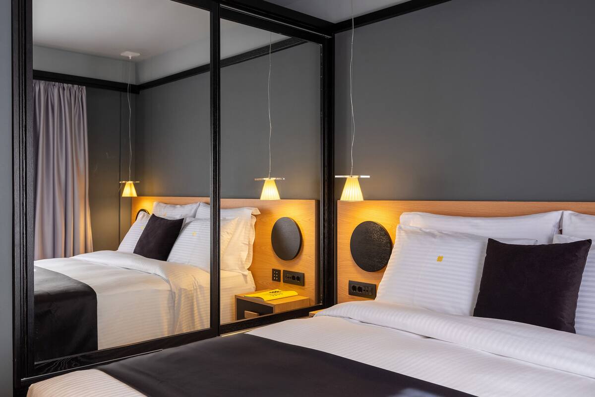 A modern hotel room with a large mirror, two beds, bedside tables, and wall-mounted lamps.