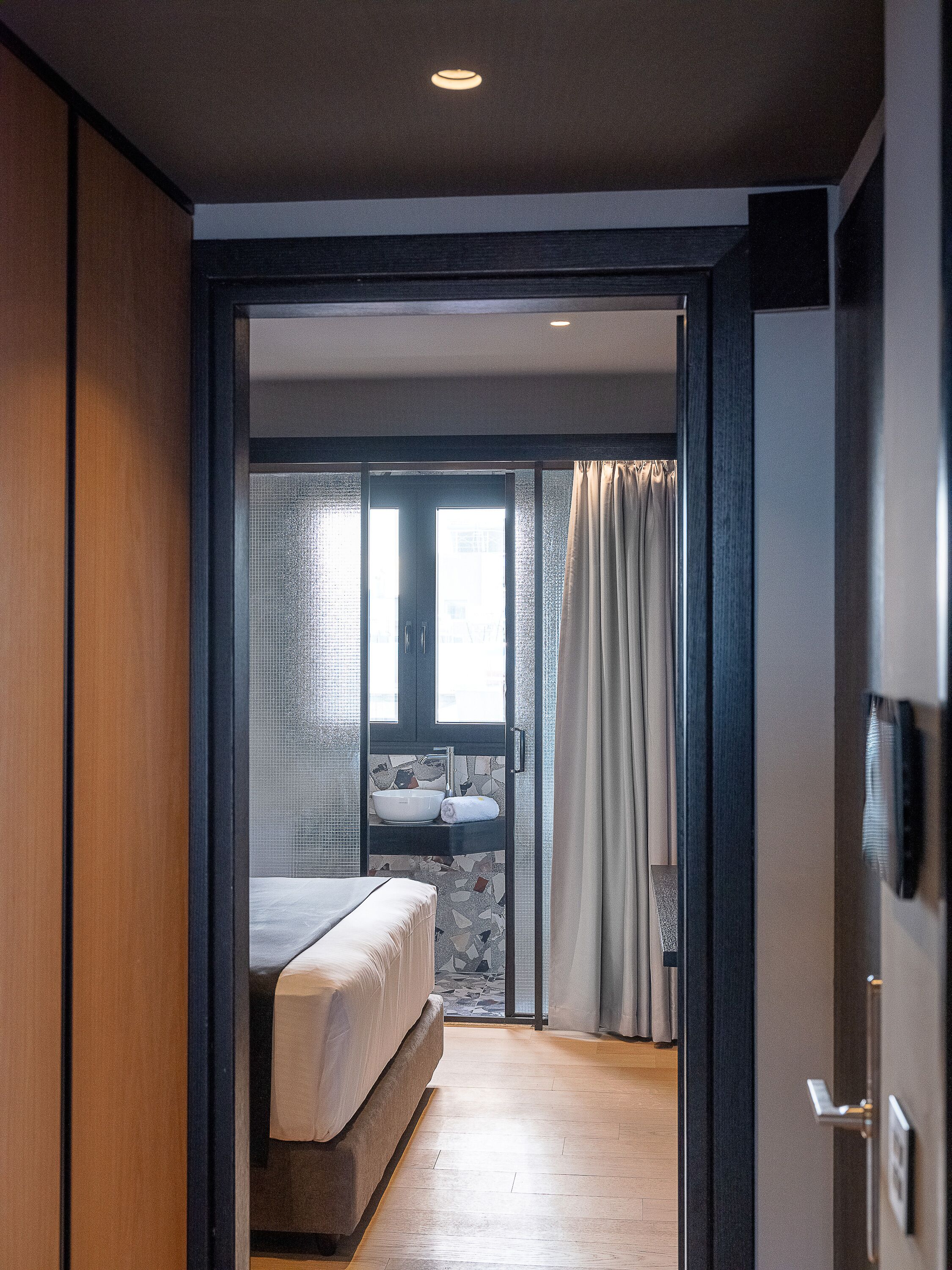A hotel room with a bed, a bathroom with a sink and a mirror, and a view through a glass door.