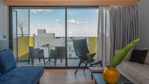 A modern living room with a sofa, a coffee table, and a chair. There is a sliding glass door leading to an outdoor area with a table and chairs. A plant is on the coffee table, and a book is on the table. - 3 Pines Design Living (Heraklion)