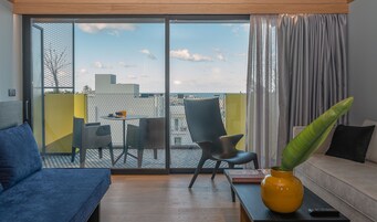 A modern living room with a sofa, a coffee table, and a chair. There is a sliding glass door leading to an outdoor area with a table and chairs. A plant is on the coffee table, and a book is on the table.
