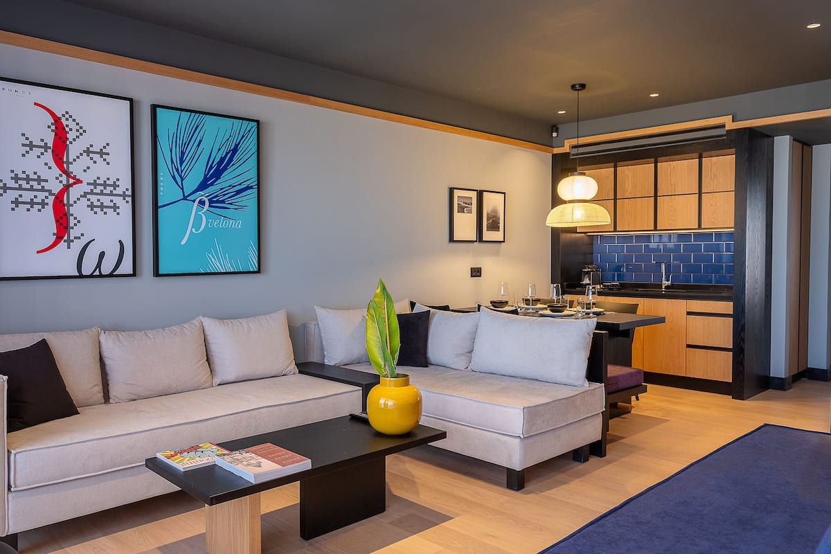 A modern living room with a sofa, coffee table, and a dining area with a kitchen in the background.