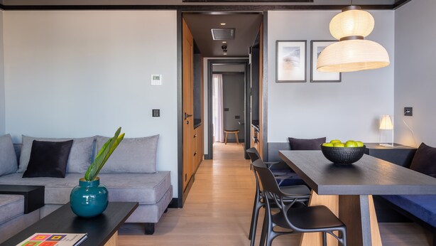 A modern living room with a sofa, coffee table, and dining area. There is a hallway leading to another room. - 3 Pines Design Living (Heraklion)
