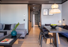 A modern living room with a sofa, coffee table, and dining area. There is a hallway leading to another room.