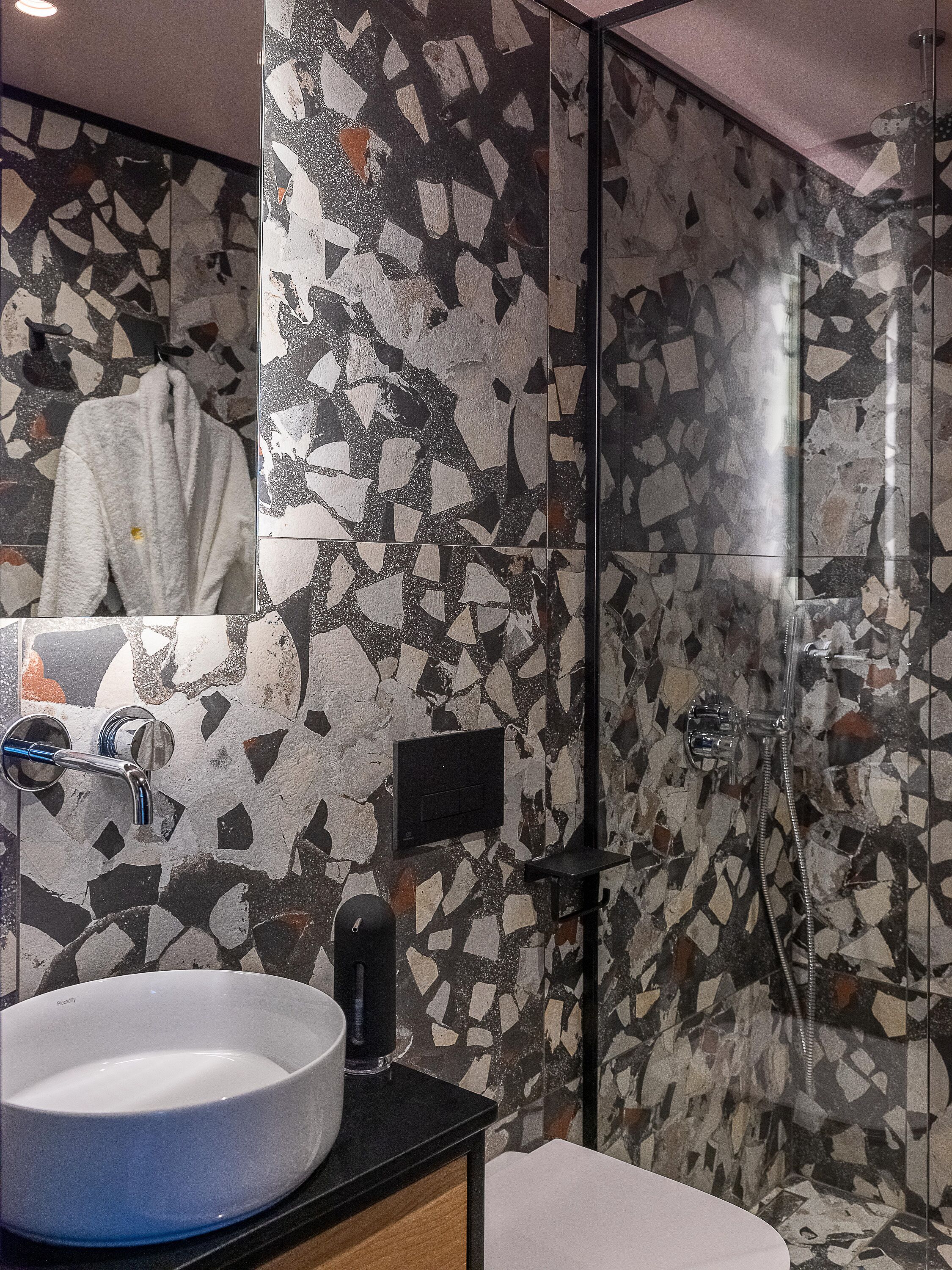 A bathroom with a large sink, a mirror, a towel rack, a shower, and a mosaic wall.