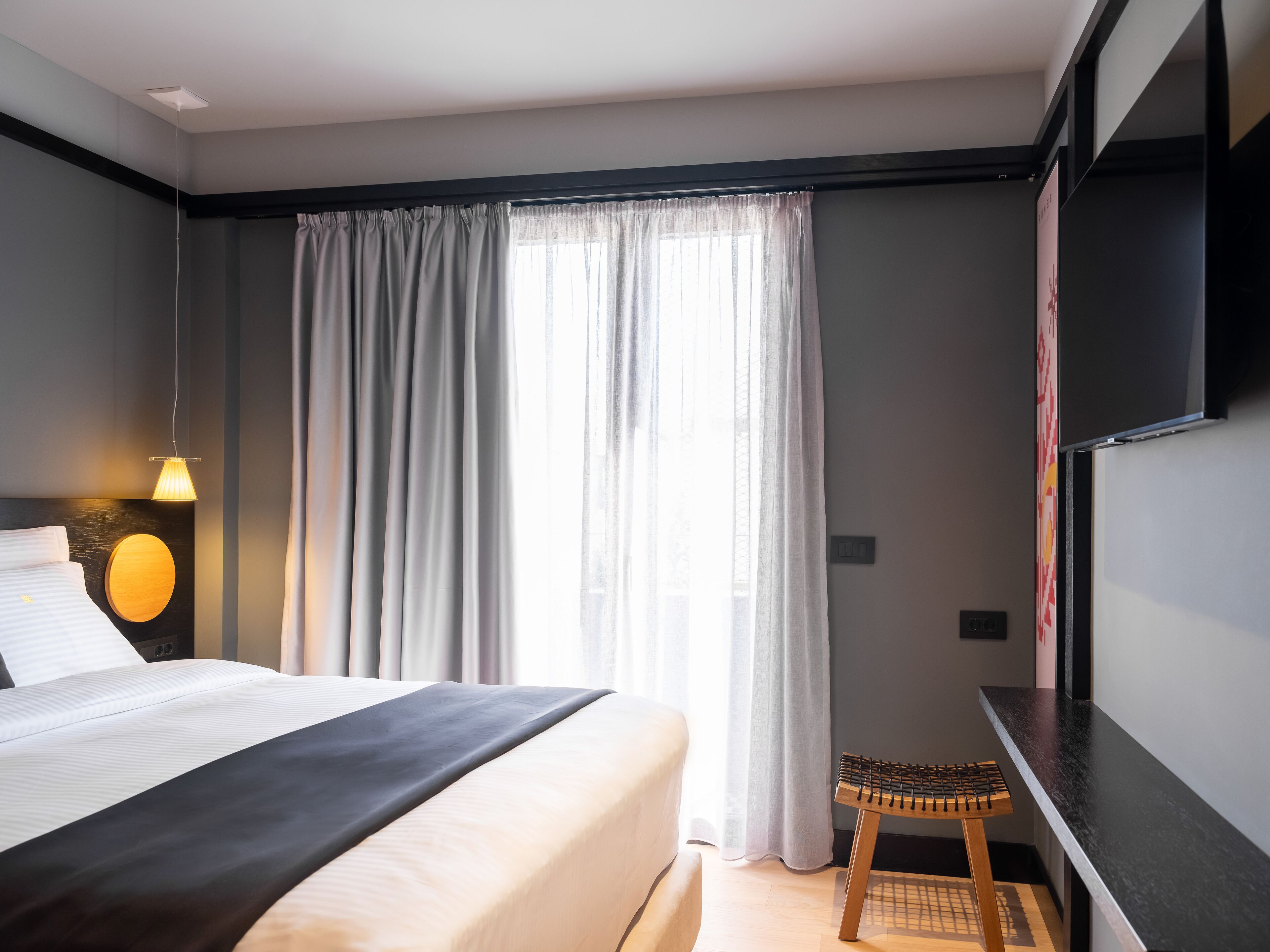 A modern hotel room with a large bed, a desk, and a window with curtains.