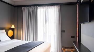 A modern hotel room with a large bed, a desk, and a window with curtains.