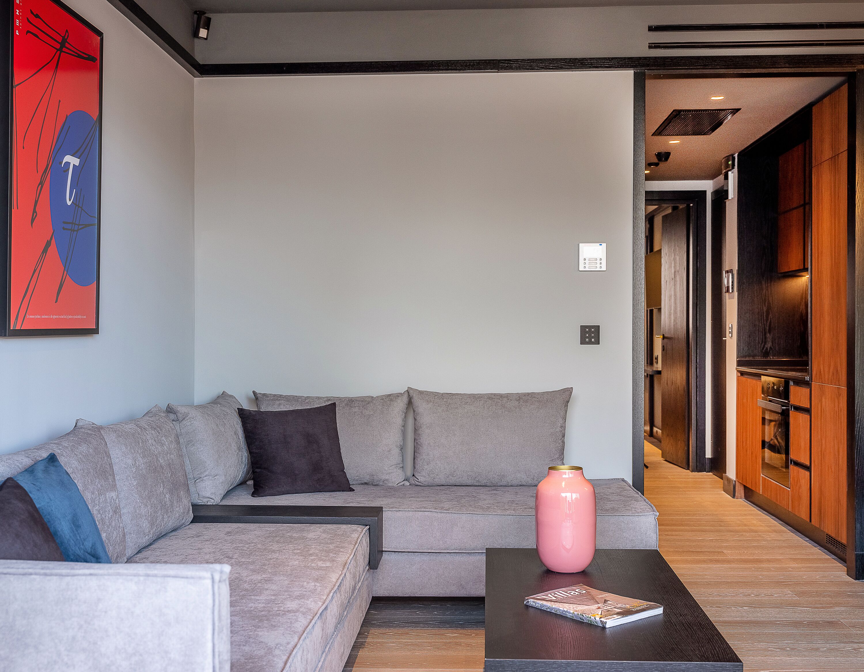 A modern living room with a grey sofa, a coffee table with a book, and a pink vase.