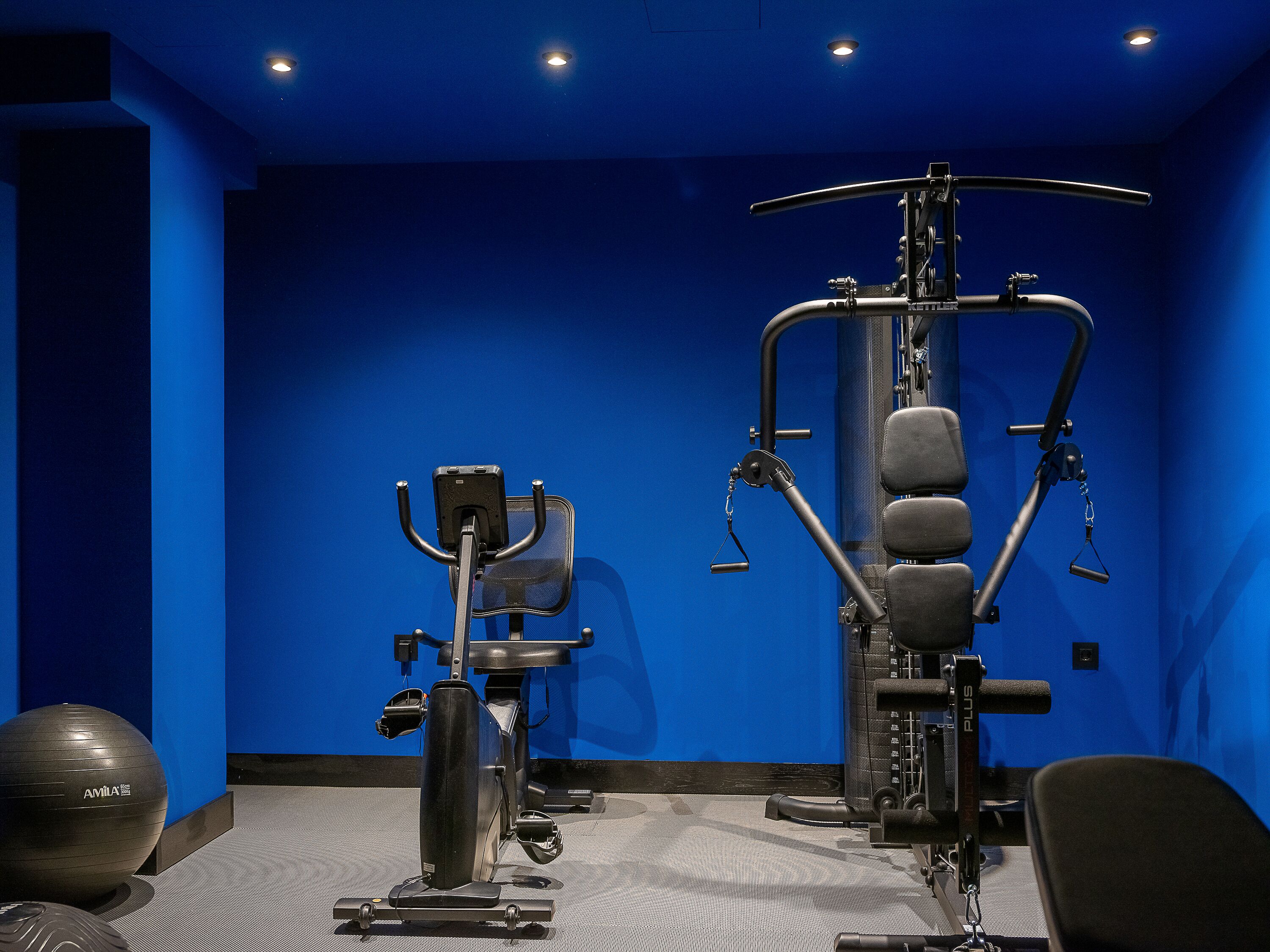 A gym with exercise equipment, a blue wall, and a ceiling with lights.