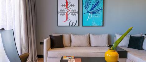 Ein modernes Wohnzimmer mit Sofa, Couchtisch und Sessel. Zwei gerahmte Kunstwerke sind an der Wand zu sehen.