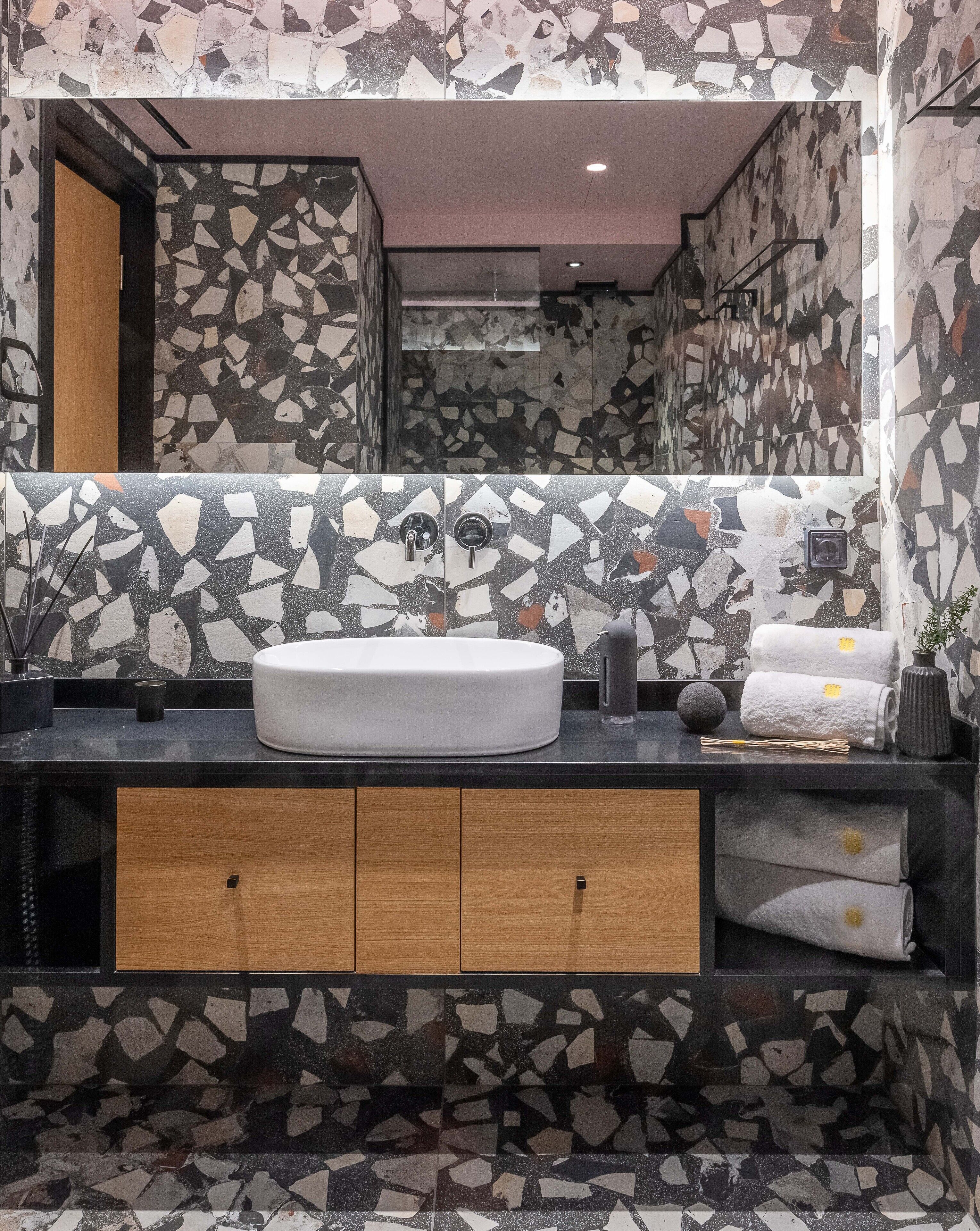 A bathroom with a large mirror, a white sink, and a mosaic tile backsplash.