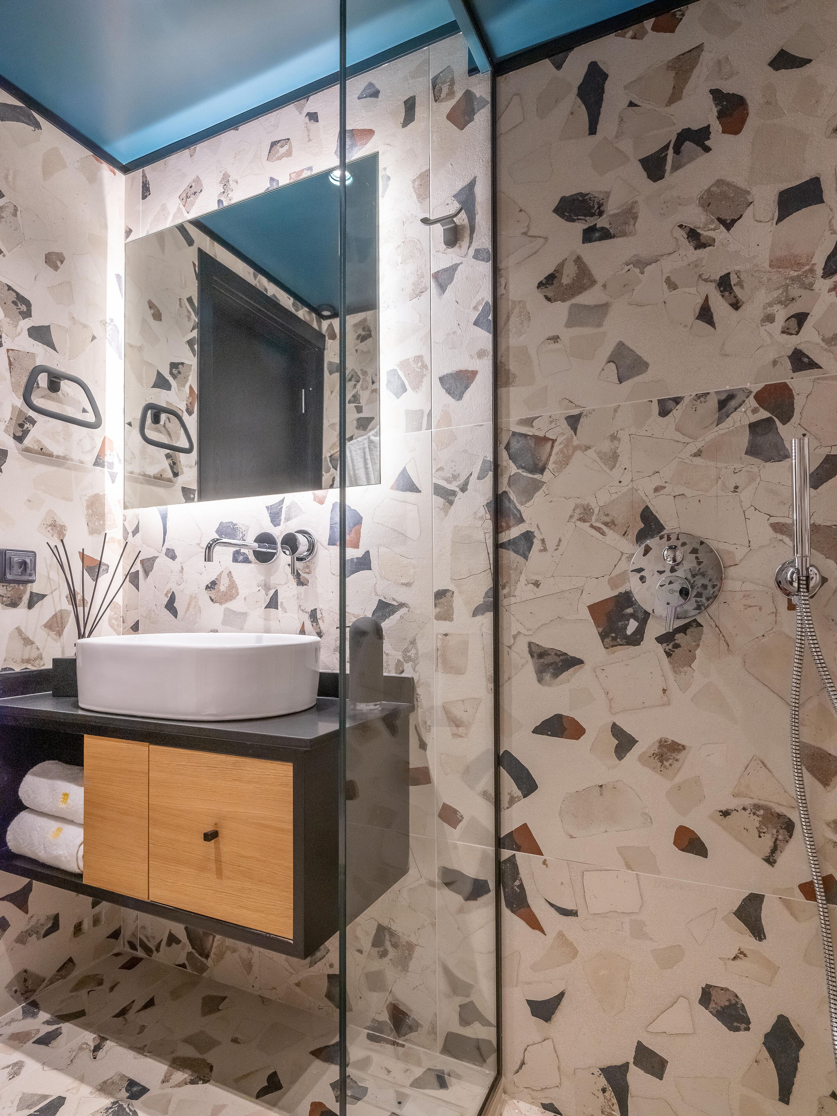 A bathroom with a modern design, featuring a large mirror, a sink, and a shower area with a unique mosaic tile pattern.