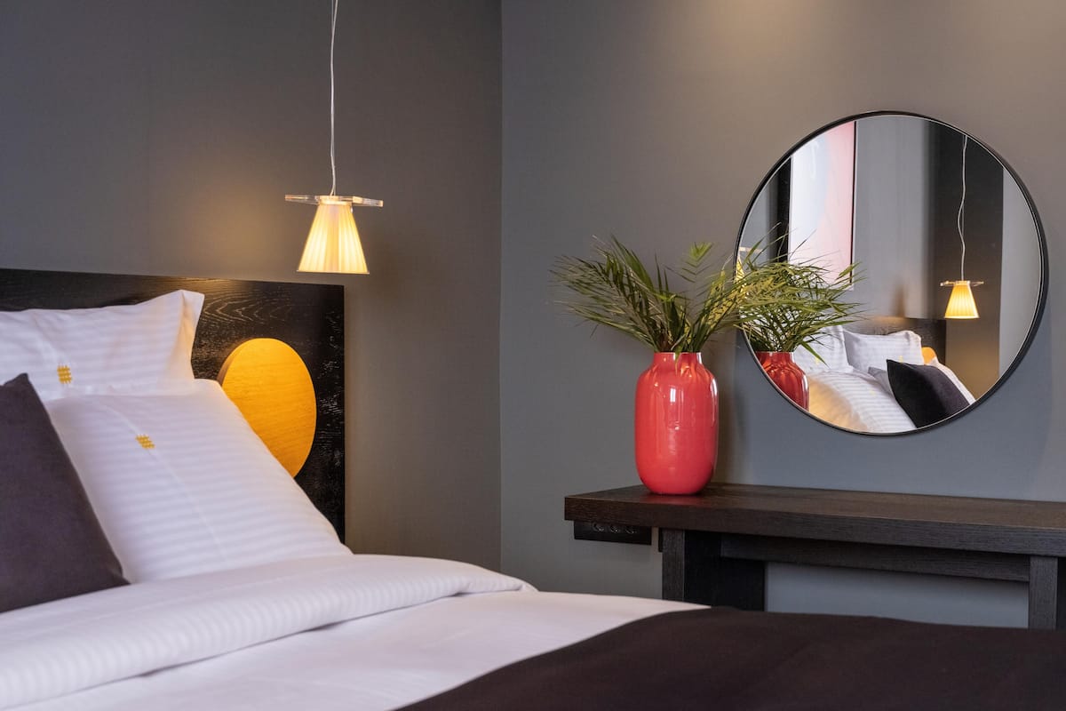 A modern bedroom with a bed, bedside table, and a round mirror on the wall.