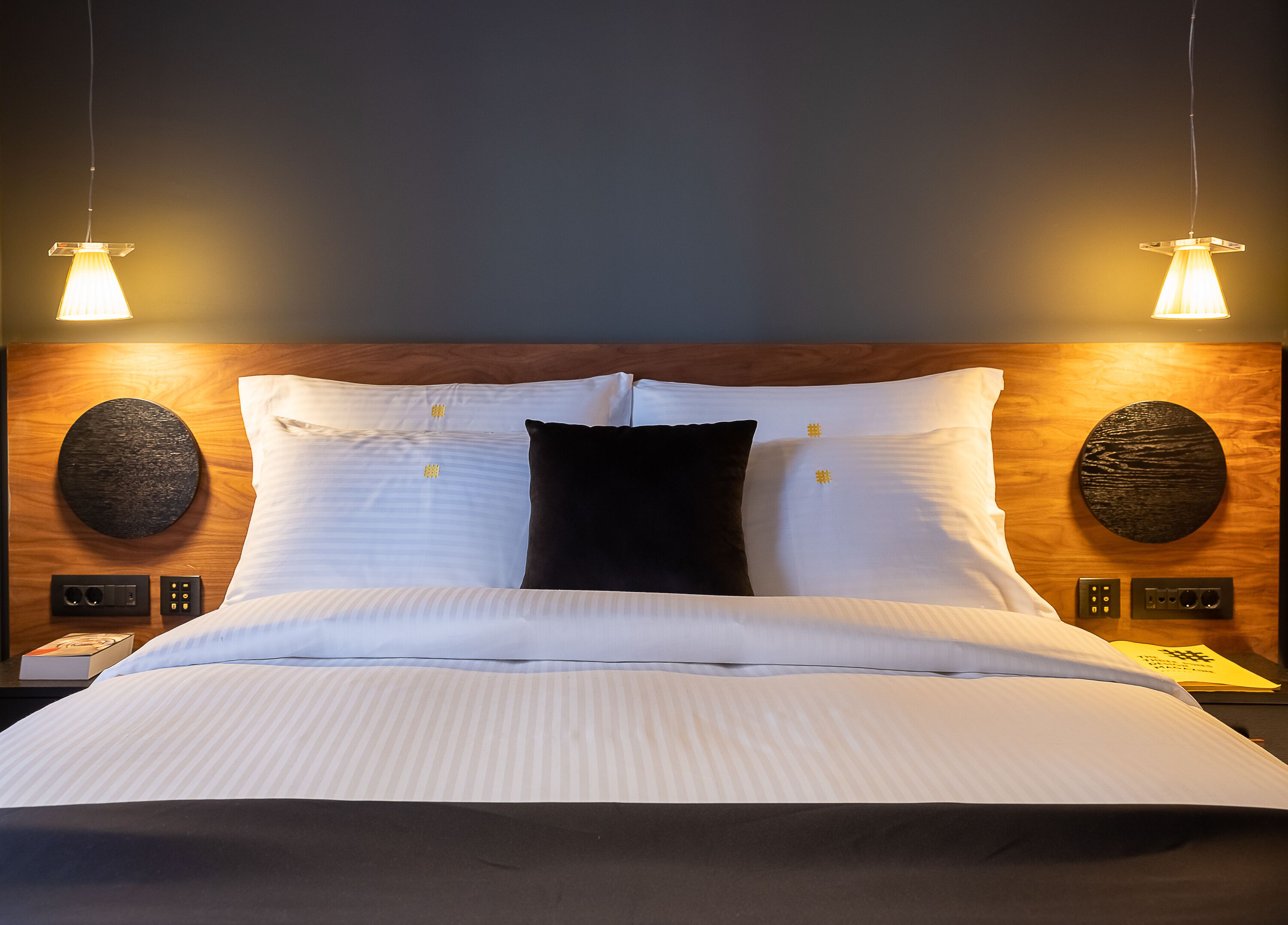 A neatly made bed with white linens, two black pillows, and a wooden headboard with circular wall decorations.