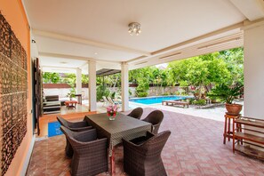 Un patio al aire libre con una mesa y sillas, una piscina y abundante vegetación.