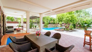 Ein überdachter Patio-Bereich mit Pool, Korbmöbeln und einem Tisch mit Blumenvase.