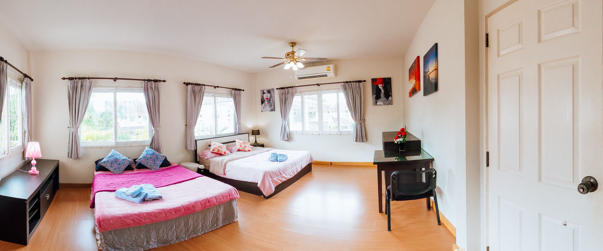 A bedroom with two beds, a desk, a chair, and a ceiling fan.