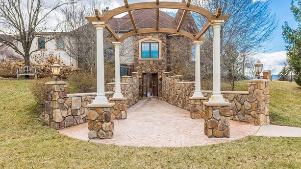 A stone pathway leading to a house with a stone facade and a wooden pergola entrance.