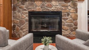 A stone fireplace with a black surround, flanked by two grey armchairs and a small table with a plant.