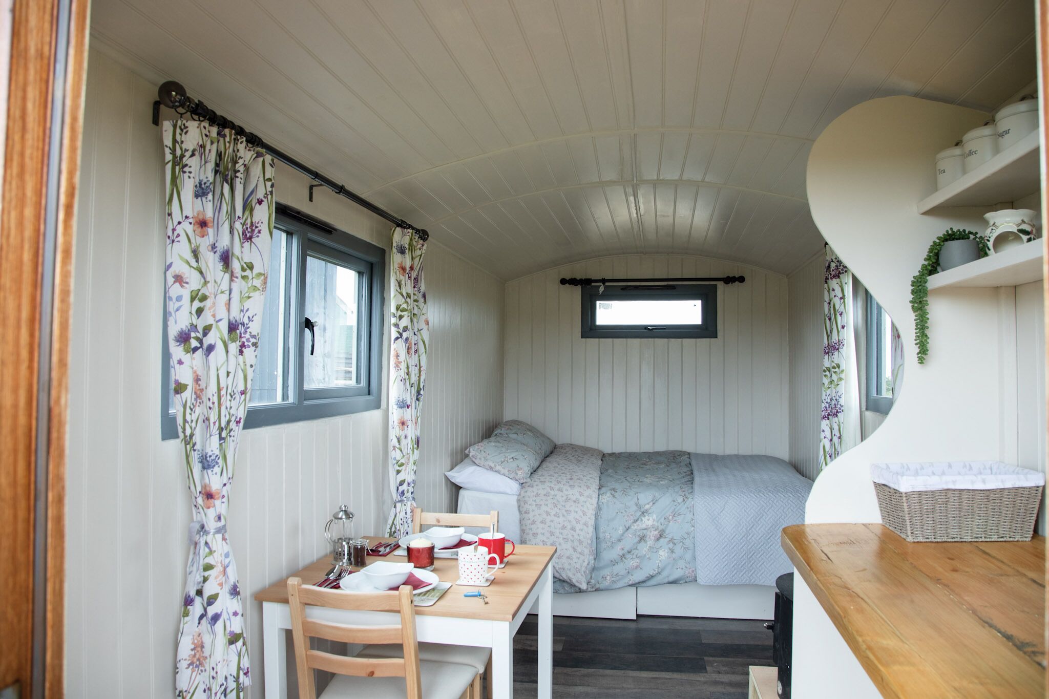 A compact, well-lit room with a bed, a small table with chairs, and a window with curtains.
