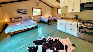 Une chambre avec deux lits, un coin cuisine et un tapis en peau de vache.