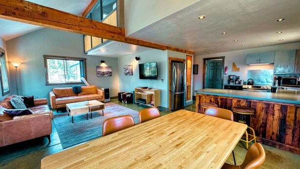 Un vaste espace de vie comprenant une salle à manger avec une table en bois, des canapés et une cuisine équipée d’appareils électroménagers modernes.