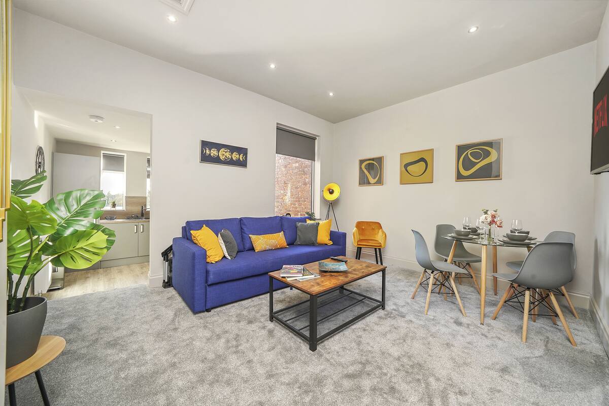 A modern living room with a blue sofa, a coffee table, and a dining area with chairs and a table.
