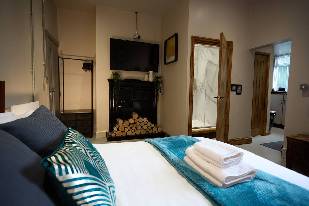 A hotel room with a bed, a TV mounted on the wall, a fireplace, and a door leading to another room.