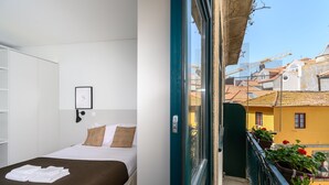 A hotel room with a bed, a framed picture on the wall, and a balcony with potted plants and a view of the cityscape. - Maria da Sé Historic House (Porto)