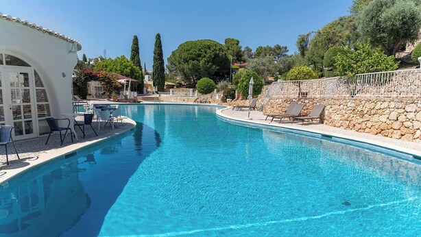 A clear blue swimming pool with lounge chairs and a stone wall on one side. - C22 Quinta do paraiso Superbly Appointed and Furnished Bungalow (Carvoeiro)