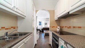 A narrow kitchen with white cabinets, a granite countertop, and a central island. - C22 Quinta do paraiso Superbly Appointed and Furnished Bungalow (Carvoeiro)