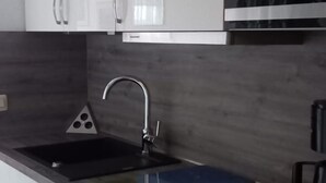 A modern kitchen with white cabinets, a stainless steel sink, and a built-in oven. - Vacation apartment in house Norderney No.24 (Dornum)
