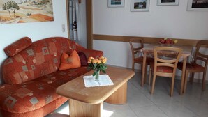 A living room with a sofa, a coffee table, and a dining area with chairs and a table. - Vacation apartment in house Norderney No.24 (Dornum)