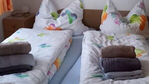 A hotel room with two beds, each with colorful pillows and a blue bedspread. There is a painting on the wall above the beds. - Vacation apartment in house Norderney No.24 (Dornum)
