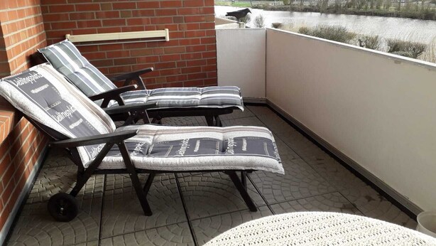 A balcony with two lounge chairs and a round table, overlooking a body of water and a residential area. - Vacation apartment in house Norderney No.24 (Dornum)
