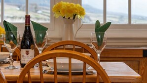 Une table à manger dressée avec des verres à vin, une bouteille de vin de Rasteau et un vase rempli de fleurs jaunes.
