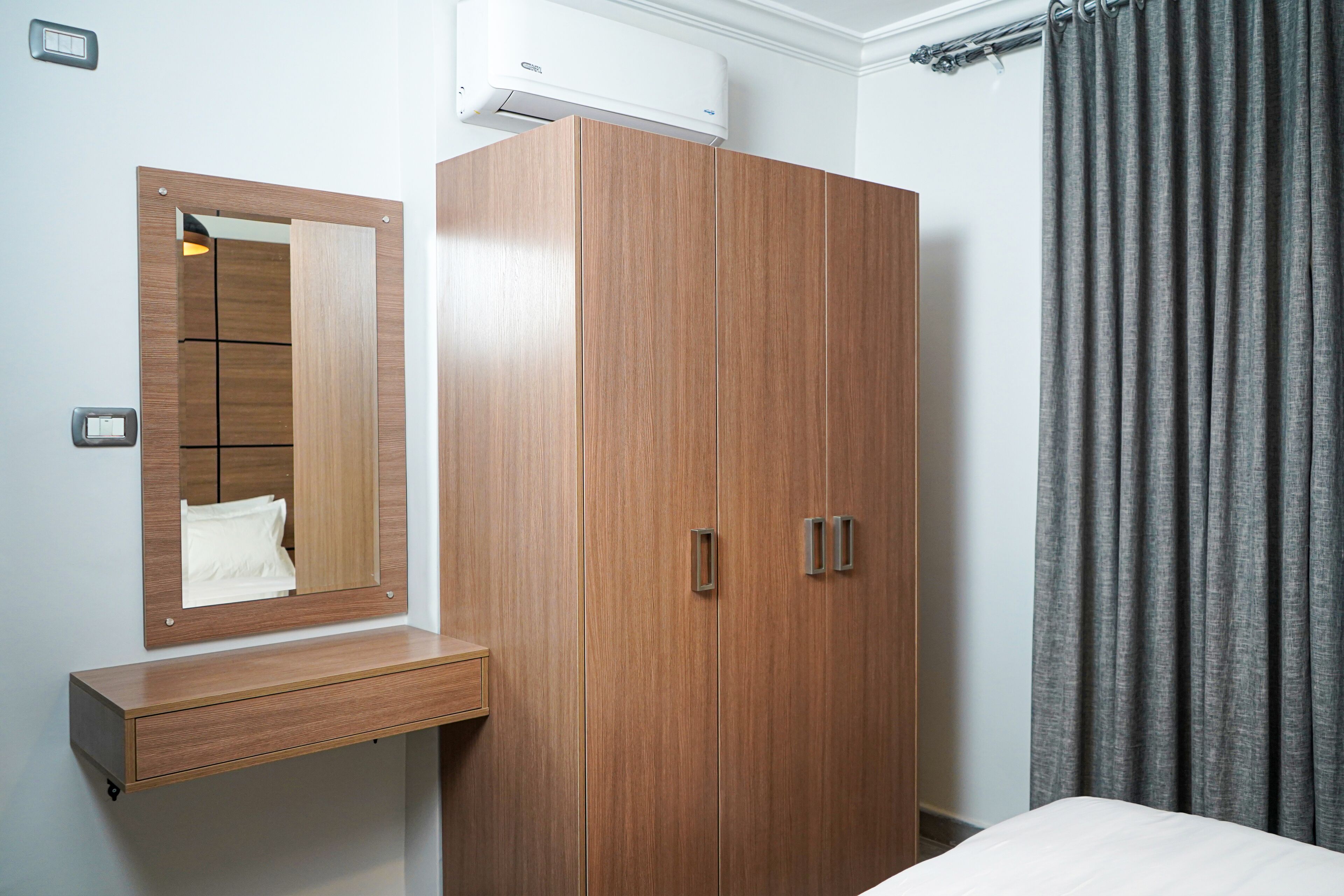 Una camera da letto con un'armadio in legno, uno specchio, un comodino e tende grigie.