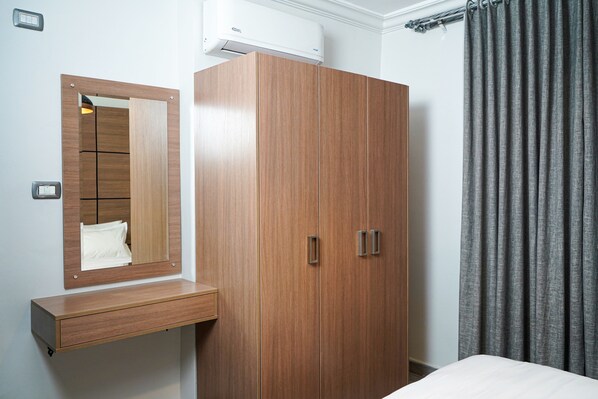 A bedroom with a wooden wardrobe, a mirror, a bedside table, and grey curtains.